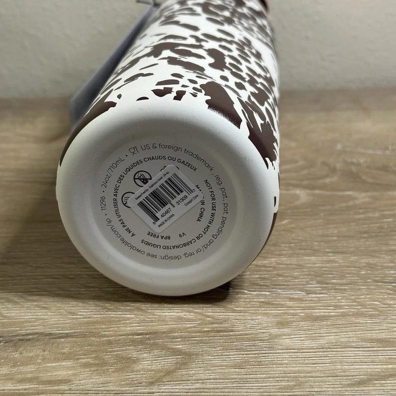 May include: A white and brown patterned water bottle. The bottle has a brown lid and a white body with brown spots. The bottom of the bottle has a label with text. The bottle is 24oz/710ml and BPA free.