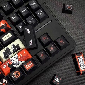 Pu&ograve; includere: Tastiera meccanica nera con tasti personalizzati. I tasti presentano opere d'arte in stile anime in rosso, bianco e nero. Alcuni tasti hanno disegni a spirale, altri mostrano illustrazioni di personaggi e testo giapponese.