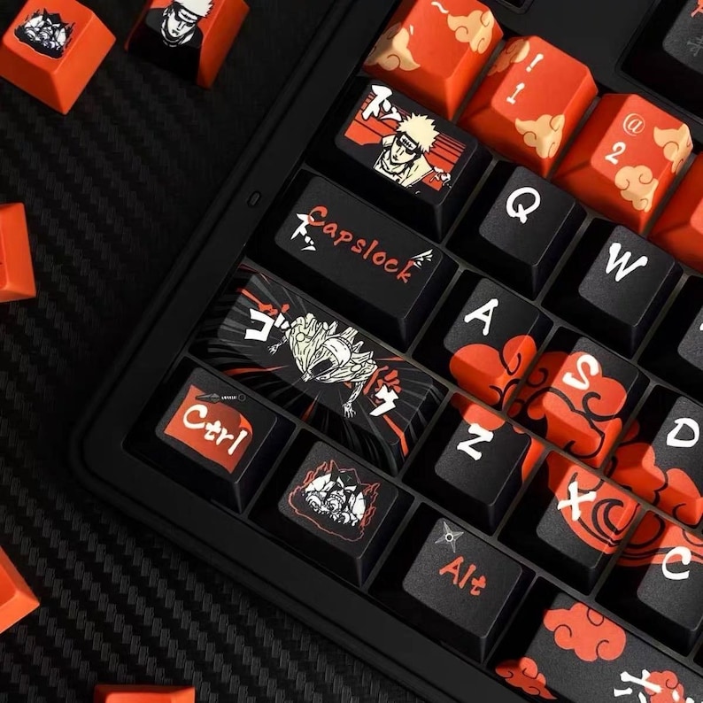 Pu&ograve; includere: Una tastiera nera con tasti personalizzati con opere d'arte in stile anime. I tasti sono un mix di nero e arancione, con varie illustrazioni di personaggi e testo giapponese. I tasti Ctrl e Capslock sono etichettati.