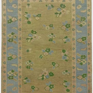 May include: Rectangular area rug with a central olive green field scattered with floral motifs in green, blue, and pink. The rug has a light blue border with floral and heart patterns, and a beige outer edge.