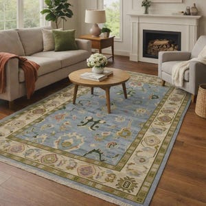 May include: A large, rectangular area rug with a light blue field and a detailed border. The rug features floral and geometric patterns in shades of green, pink, and beige. It is placed on a hardwood floor in a living room setting.