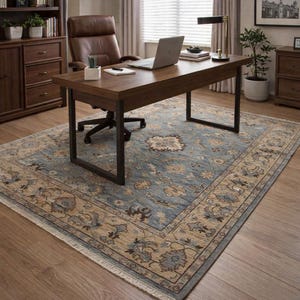 May include: A blue and beige patterned area rug with a floral design. The rug is placed under a wooden desk with a laptop, a brown leather office chair, and a wooden cabinet. The room has a window with blinds.