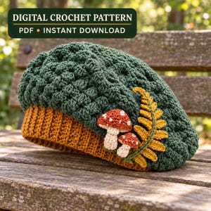 May include: A dark green crocheted beret with a mustard yellow ribbed brim. The hat features two small crocheted mushrooms with red caps and white spots, alongside a mustard yellow crocheted fern leaf. Text reads: DIGITAL CROCHET PATTERN PDF INSTANT DOWNLOAD.