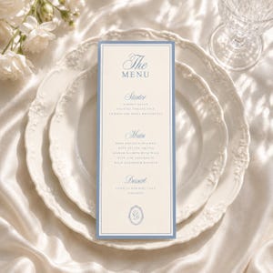 May include: A tall, rectangular menu card with a cream-colored center and a blue border. The text reads The MENU, Starter, Main, and Dessert, followed by food items and a circular monogram with the letter G at the bottom, centered on a white plate.