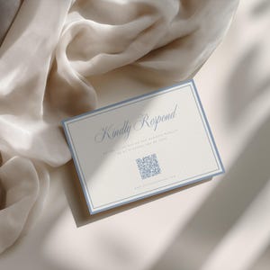 May include: A rectangular RSVP card with a light blue border on a cream background. The text reads Kindly Respond in a script font, with smaller text below and a QR code in the center. A website URL is printed at the bottom of the card.