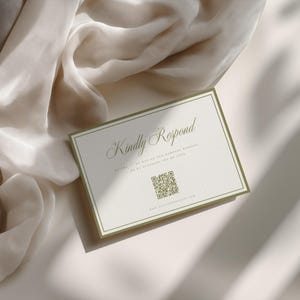 May include: A rectangular invitation card with the text "Kindly Respond" in elegant script. The card has a white background with a green border and a QR code. A soft, beige fabric is draped in the background.