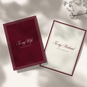 May include: Two rectangular wedding cards with double-line borders. One card is deep burgundy with white text reading "To my Wife" and "ON OUR WEDDING DAY". The other is cream with burgundy text reading "To my Husband" and "ON OUR WEDDING DAY".