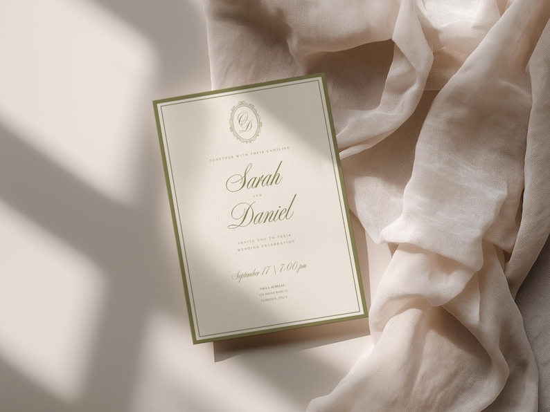 May include: A wedding invitation with a cream background and olive green border. The invitation features the names "Sarah" and "Daniel" in elegant script, along with event details. The invitation is set against a soft, draped fabric.