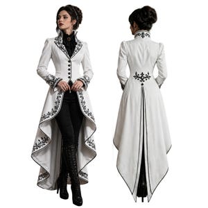 Puede incluir: Un abrigo blanco de manga larga con bordados negros y cuello alto. El abrigo tiene una botonadura frontal y una cola larga y fluida. La modelo lleva pantalones y botas negras. El diseño recuerda a la moda victoriana.