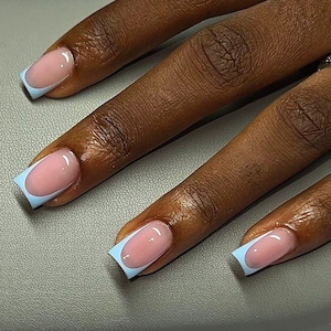 May include: Close-up of a hand with manicured nails. Each nail features a light pink base with a glossy finish, framed by a light blue border. The nails are well-shaped and the overall look is clean and stylish.