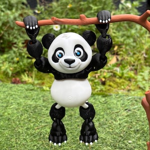 May include: A black and white articulated panda figure hanging from a brown plastic branch. The panda has a white face with black eye patches, blue eyes, and a black nose. Its limbs are black with white claw details, and its body is white.
