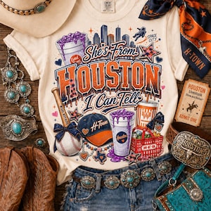 以下が含まれることがあります： 「She's From HOUSTON I Can Tell」という文字がプリントされたクリーム色のTシャツ。デザインには野球ボール、キャップ、紫色の液体が入ったカップ、買い物かご、都市のスカイラインが描かれています。Tシャツの周りにはウエスタン風のアクセサリーが配置されています。