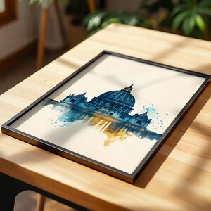 May include: A framed art print featuring a watercolour illustration of a large domed cathedral. The architectural structure is rendered in shades of deep blue and gold, with paint splatters extending from the base against a cream background.