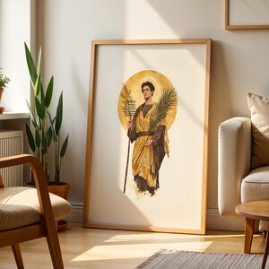 Op de afbeelding: Een ingelijste verticale wandkunstprint met een centrale afbeelding van een figuur in gouden gewaden met een aureool, die een palmtak en een staf vasthoudt. Het kunstwerk is uitgevoerd in een klassieke stijl met warme tinten.