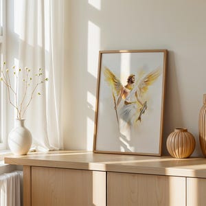 May include: A framed wall art print featuring a watercolour illustration of a winged figure with a golden halo, holding a staff in one hand and a fish in the other. The figure wears a white robe and has large, detailed golden wings spread wide.