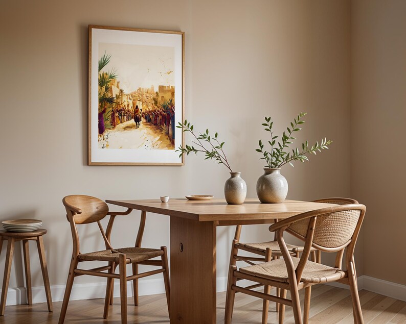 May include: A framed wall art print depicting a crowd scene with a figure on a donkey, displayed above a light wood dining table with two round ceramic vases containing green branches, and two wooden chairs with woven seats.