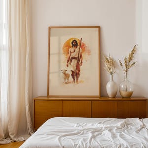 Peut inclure: Une impression d'art encadr&eacute;e de style aquarelle repr&eacute;sentant une silhouette barbue aux cheveux longs v&ecirc;tue d'une robe blanche et portant un b&acirc;ton en bois, marchant aux c&ocirc;t&eacute;s d'un petit agneau blanc. Un grand soleil orange brille derri&egrave;re.