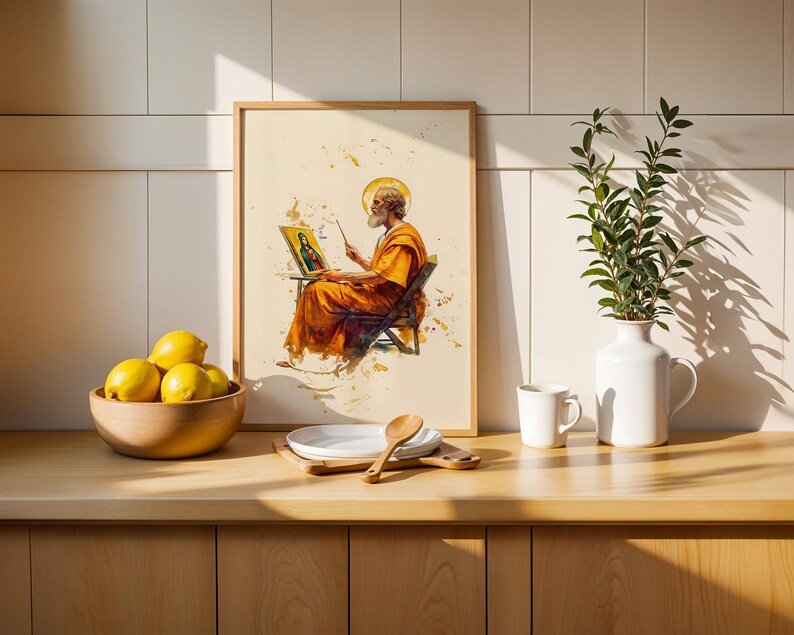May include: A framed art print featuring a bearded figure in orange robes painting a portrait of a religious icon. The print is displayed on a counter next to a wooden bowl of yellow lemons, a white plate with a wooden spoon, and a white vase with greenery.