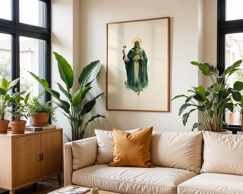 May include: A framed wall art print featuring a bearded figure in a green robe and crown, holding a shamrock and a staff, with a golden halo. The artwork is displayed in a thin wooden frame on a plain wall above a beige sofa with a mustard pillow.