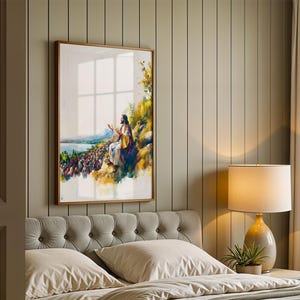May include: A framed vertical wall art print featuring a watercolor-style illustration of a figure in robes sitting on a hillside, gesturing toward a large crowd gathered below near a body of water, with yellow and green foliage accents.