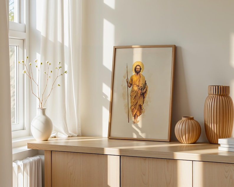 Op de afbeelding: Een ingelijste verticale print met een aquarelillustratie van een bebaard figuur in gouden gewaden die een lange staf vasthoudt, met een cirkelvormige halo achter het hoofd. Het kunstwerk wordt gepresenteerd in een licht houten frame op een oppervlak.