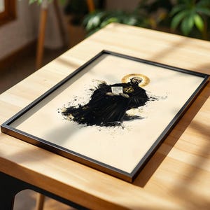 May include: A framed print featuring a stylized illustration of a bearded figure in a black robe with a gold halo, holding a small white document with a cross symbol. The artwork uses black ink splatters on a cream background within a black frame.