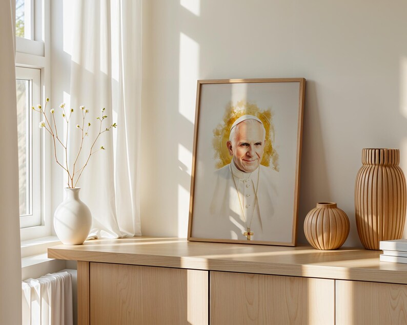 May include: A framed portrait print featuring a watercolour-style illustration of Pope John Paul II wearing a white cassock and a gold pectoral cross, set against a soft golden yellow background with a light wooden frame border.