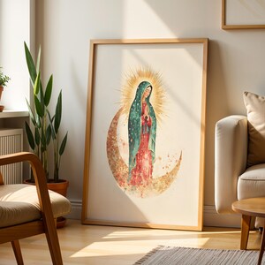 May include: A framed wall art print featuring a watercolor illustration of the Virgin of Guadalupe. She wears a teal cloak with gold stars over a red dress, standing on a crescent moon with a radiant golden sunburst halo behind her head.