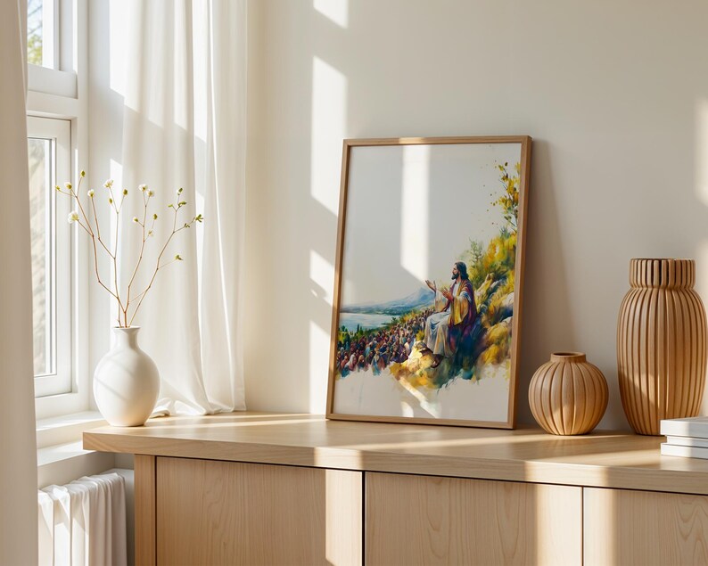 May include: A framed watercolour-style print depicting a figure in robes seated on a hillside, gesturing towards a large crowd gathered below near a body of water. The artwork features vibrant yellow, blue, and green tones with a white background.
