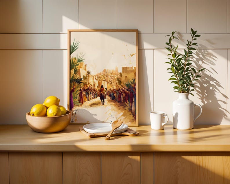 May include: A framed wall art print depicting a historical scene of a figure riding a donkey through a crowd in a desert city. The artwork features warm, muted tones and is displayed on a wooden counter next to a bowl of lemons and a white vase.