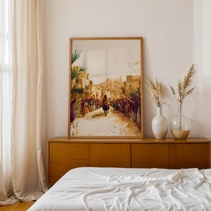 May include: A framed vertical wall art print depicting a historical scene with a figure riding a donkey through a crowd of people in a desert city. The artwork features warm earth tones, including shades of brown, tan, and gold, with splashes of colour in the clothing of the crowd members.