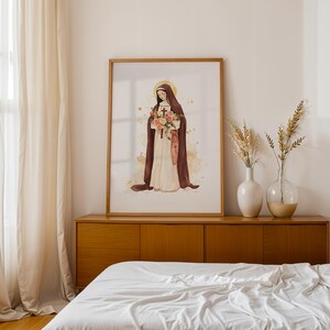 May include: A framed wall art print featuring a watercolor illustration of a figure in a brown habit and white robe holding a bouquet of pink and orange flowers, with a gold halo and a small cross symbol on the garment against a white background.