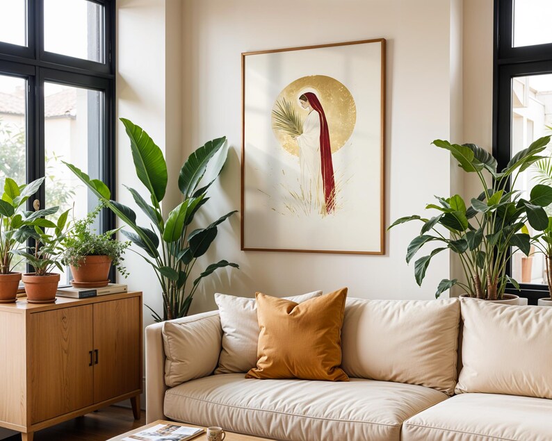 Puede incluir: Una l&aacute;mina de arte enmarcada que muestra una figura con t&uacute;nica blanca y capa roja larga, sosteniendo una hoja de palma verde sobre un fondo de halo circular dorado. La obra est&aacute; expuesta en una pared lisa sobre un sof&aacute; beige con un coj&iacute;n.