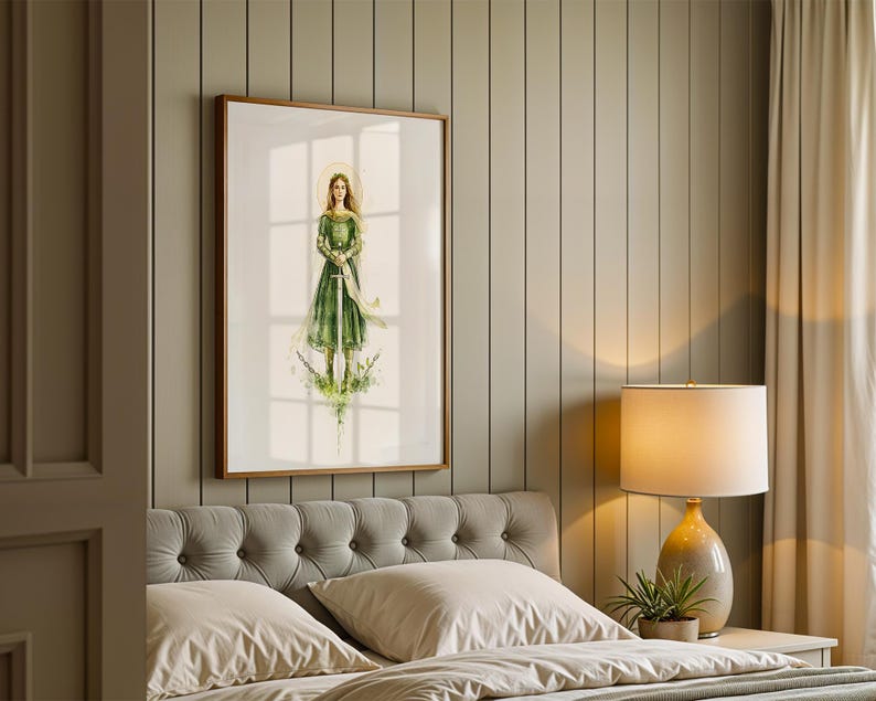 Op de afbeelding: Een ingelijste kunstdruk met een aquarelillustratie van een persoon met lang haar in een groene jurk die een zwaard vasthoudt. De figuur staat tussen groen gebladerte met een gouden halo-effect achter het hoofd op een witte achtergrond.