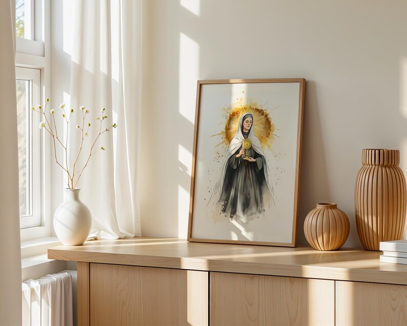 Op de afbeelding: Een ingelijste print in aquarel-stijl met een figuur in een donker gewaad en witte sluier die een gouden monstrans vasthoudt. De figuur is gecentreerd tegen een stralende, cirkelvormige gouden halo met verfspatten in een licht houten lijst.