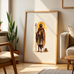 Op de afbeelding: Een ingelijste kunstdruk met een centrale illustratie van een bebaard figuur in een bruin gewaad en sandalen, die een hoge houten staf vasthoudt. Een gouden cirkelvormige halo gloeit achter het figuur en een hoed met brede rand ligt op de grond.