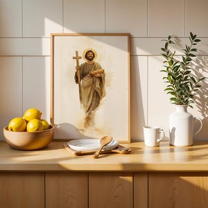 Peut inclure: Une impression encadr&eacute;e de style aquarelle repr&eacute;sentant une figure barbue en robe tenant une croix en bois et une miche de pain, pos&eacute;e sur un comptoir avec un bol en bois de citrons jaunes, une assiette blanche, une cuill&egrave;re en bois, un mug blanc et un vase blanc avec de la verdure.