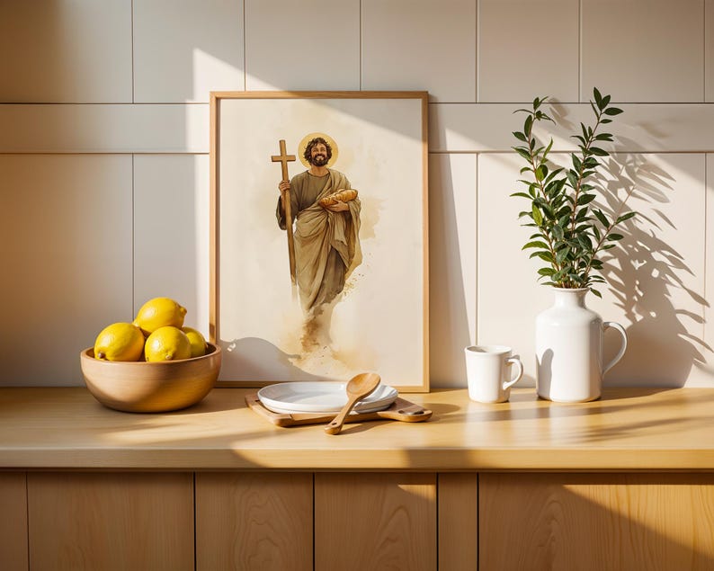 Peut inclure: Une impression encadr&eacute;e de style aquarelle repr&eacute;sentant une figure barbue en robe tenant une croix en bois et une miche de pain, pos&eacute;e sur un comptoir avec un bol en bois de citrons jaunes, une assiette blanche, une cuill&egrave;re en bois, un mug blanc et un vase blanc avec de la verdure.
