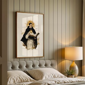 May include: A framed wall art print depicting a figure in a black and white religious habit, holding an open book with a glowing golden sunburst halo behind the head, featuring ink-splatter accents and a rosary hanging from the waist.