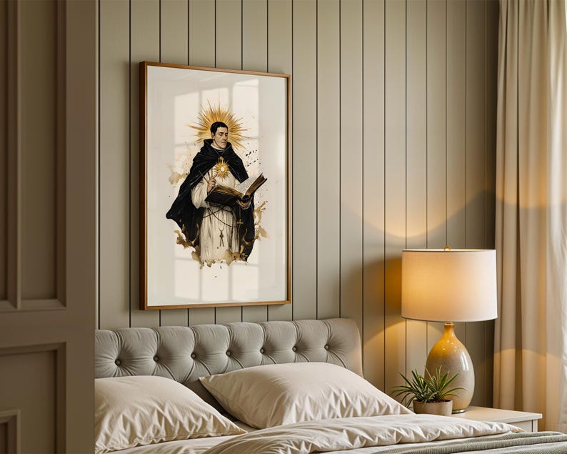 May include: A framed wall art print depicting a figure in a black and white religious habit, holding an open book with a glowing golden sunburst halo behind the head, featuring ink-splatter accents and a rosary hanging from the waist.