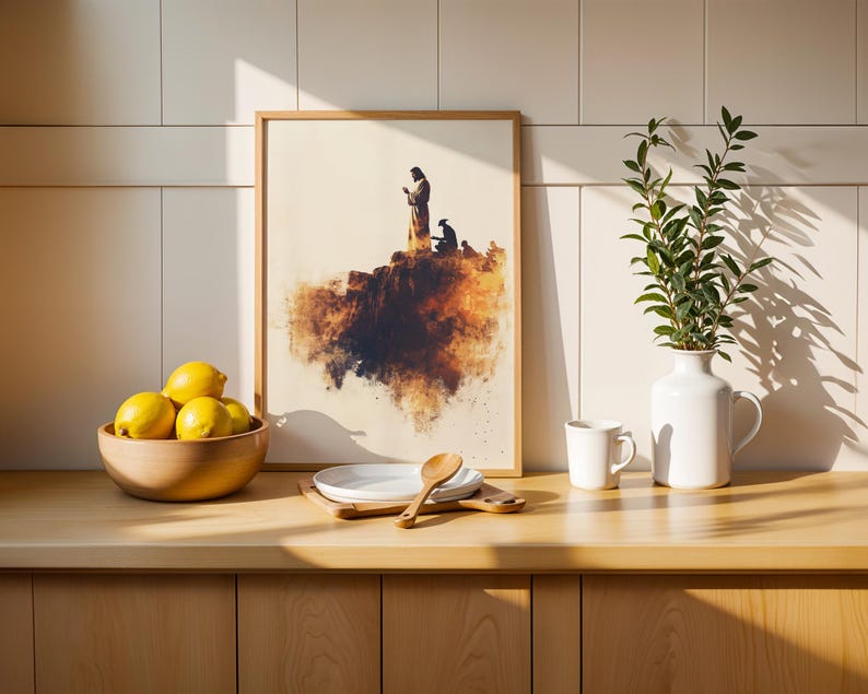 May include: A framed print featuring a silhouette of a figure standing on a cliff edge, displayed on a wooden counter with a bowl of yellow lemons, a stack of white plates, a wooden spoon, a white ceramic mug, and a white vase with green leaves.