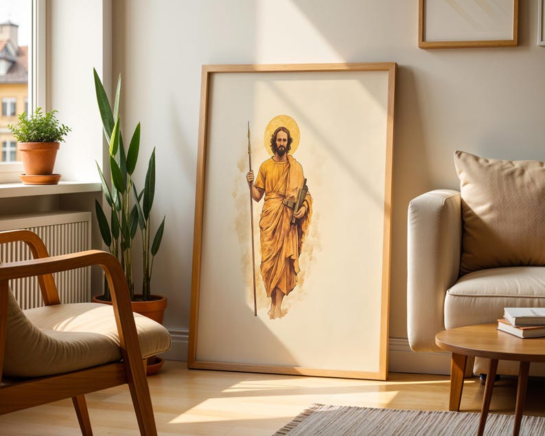Op de afbeelding: Een ingelijste verticale wandkunstprint met een aquarelillustratie van een bebaard figuur in gouden gewaden die een lange speer en een boekrol vasthoudt, tegen een lichtcr&egrave;mekleurige achtergrond met een cirkelvormige halo achter het hoofd.