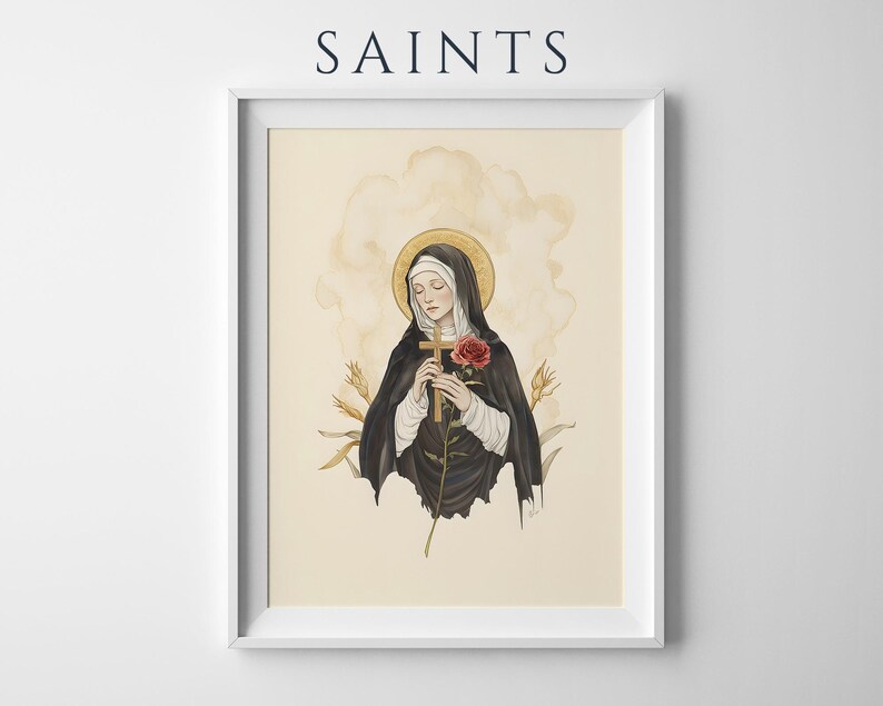 Op de afbeelding: Een ingelijste kunstdruk getiteld SAINTS met een illustratie van een figuur in een zwart habijt en witte sluier, die een houten kruis en een rode roos vasthoudt. De figuur heeft een gouden halo tegen een cr&egrave;mekleurige achtergrond met korenaren.