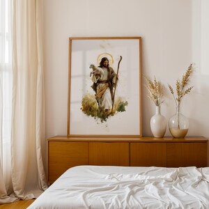 May include: A framed watercolour-style print depicting a figure with long hair and a beard, wearing robes and holding a small lamb in one arm while carrying a wooden staff in the other, set against a background of golden grass and a halo.