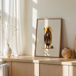 May include: A framed wall art print featuring a watercolour-style illustration of a figure with a beard, wearing a brown robe and holding a tall wooden staff. A golden circular halo is positioned behind the head of the figure, who stands barefoot.