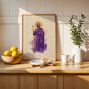 May include: A framed vertical print featuring a watercolor-style illustration of a bearded figure in a purple robe holding a staff, with a golden halo. The artwork is displayed on a wooden counter next to a bowl of yellow lemons and a white vase.