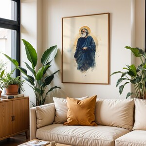 May include: A framed wall art print featuring a watercolor-style illustration of a bearded figure in a dark blue robe with a golden halo. The artwork is displayed on a light-colored wall above a beige sofa with a mustard yellow throw pillow.