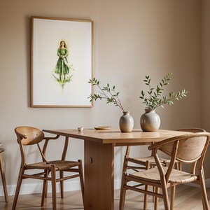 Op de afbeelding: Een ingelijste aquarelillustratie van een figuur in een groene jurk die een zwaard vasthoudt, boven een houten eettafel met twee keramische vazen met groene takken, vergezeld door drie houten stoelen met gevlochten zittingen en een krukje.