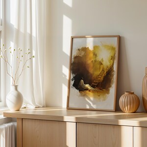 Op de afbeelding: Een ingelijste rechthoekige kunstdruk met een illustratie in aquarel-stijl van een figuur die rust bij een ladder die naar een fel licht leidt. Het kunstwerk gebruikt tinten bruin, goud en wit, weergegeven in een lichtgekleurde houten lijst.