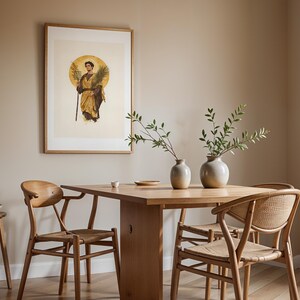 Puede incluir: Una mesa de comedor de madera con tres sillas de asiento trenzado y respaldo curvo. Dos jarrones de cer&aacute;mica con ramas verdes se sit&uacute;an sobre la mesa. Un cuadro enmarcado de una figura con una rama de palma cuelga en la pared.